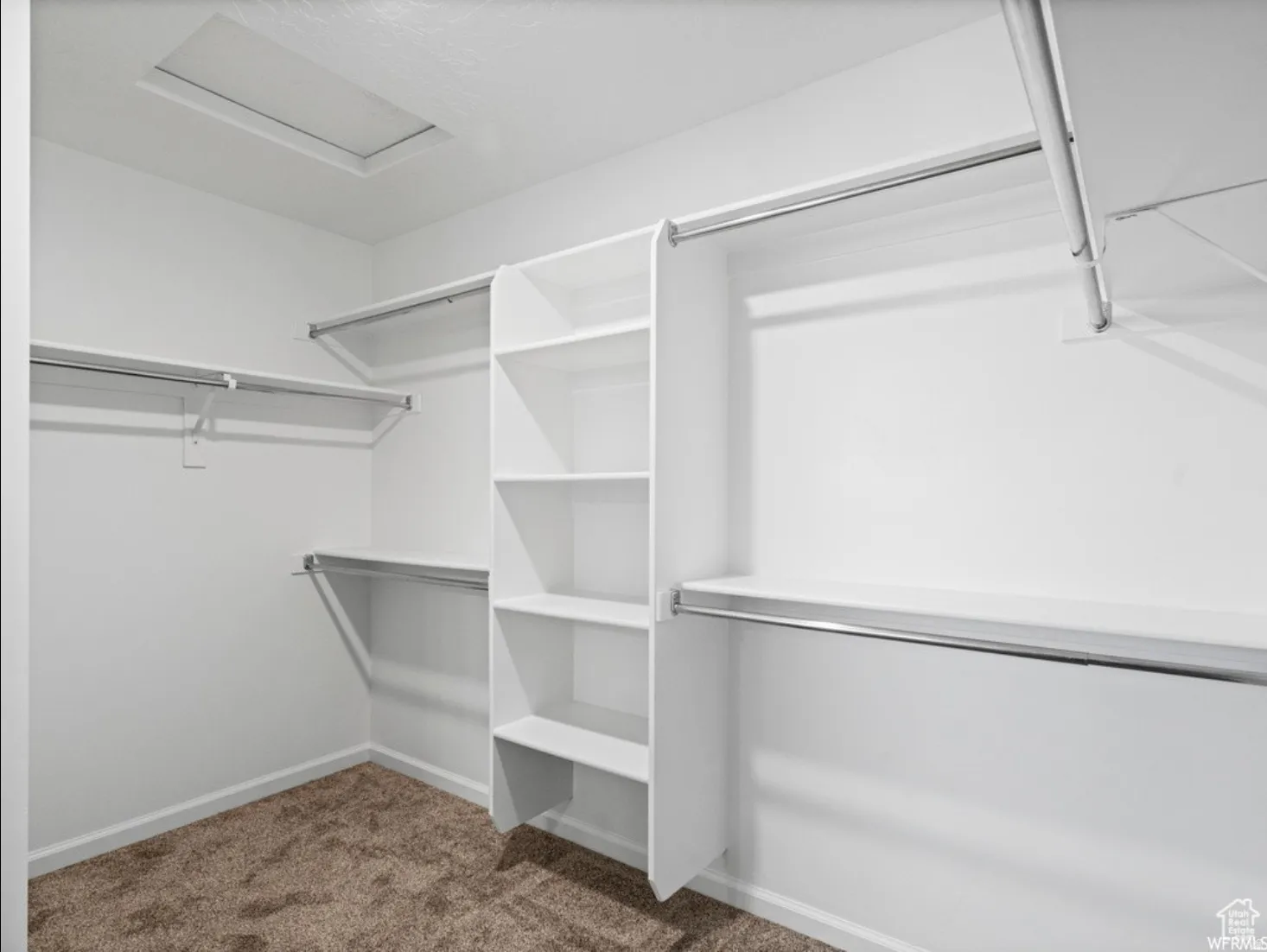Spacious closet featuring built-in shelving, multiple hanging rods, white walls, and neutral-toned carpet flooring