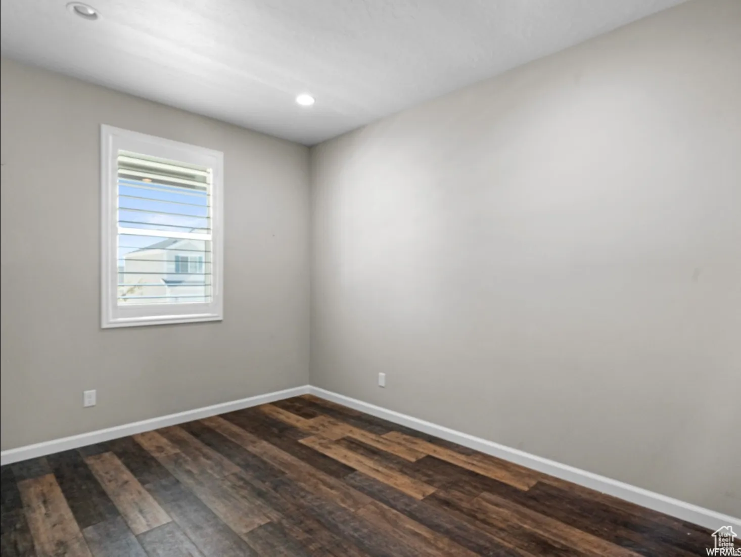 Neutral-toned room featuring a single window with white louvered blinds, dark wood-finish flooring, and recessed ceiling lighting