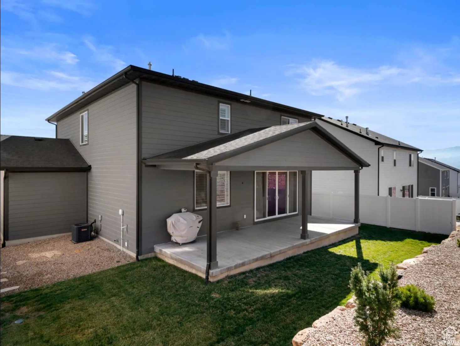 Rear exterior featuring a covered patio with a concrete slab, sliding glass doors, horizontal siding, and a fenced yard with grass and gravel landscaping