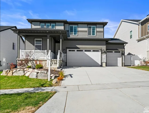 Modern two-story residence featuring a covered front porch, white railing, and a two-car garage with stone accents