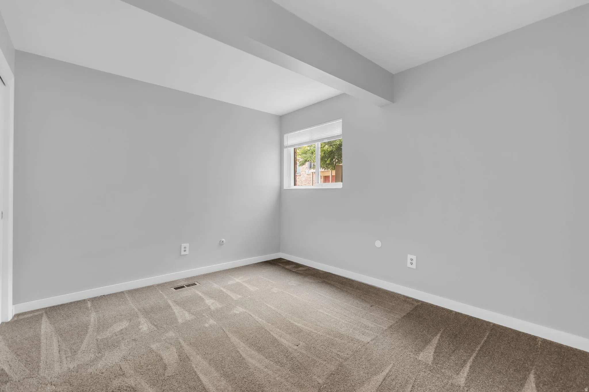 Room featuring neutral gray wall paint, patterned carpeting, white baseboards, and a single window with white trim