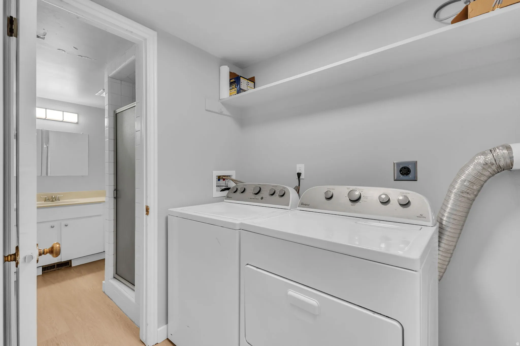 Dedicated laundry area featuring a washer and dryer, an overhead storage shelf, and direct access to a full bathroom