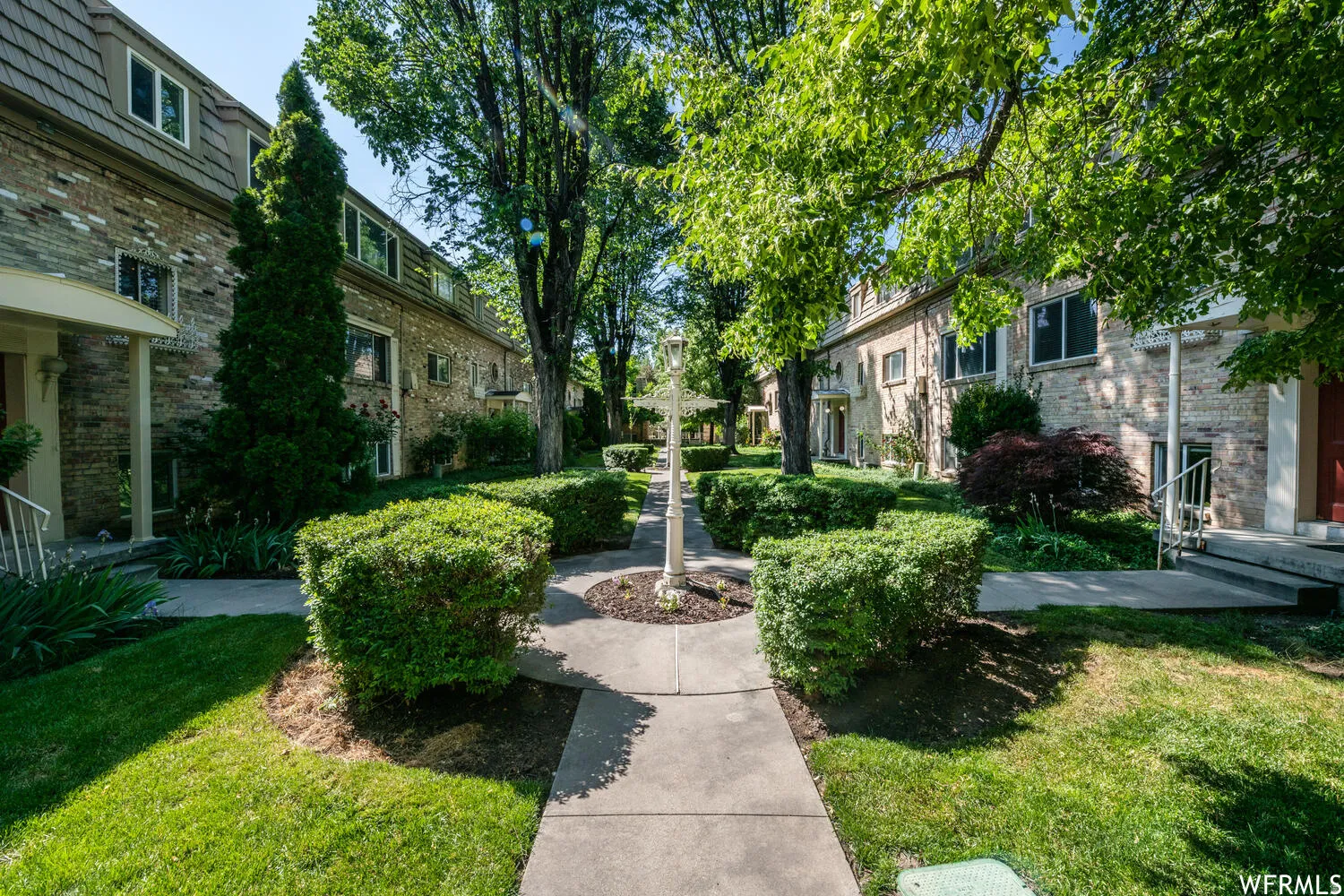 Landscaped courtyard featuring a central pathway, mature trees, manicured lawns, and established shrubbery