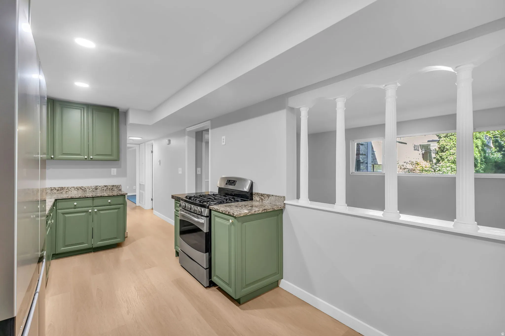 Kitchen area featuring olive-green cabinetry, granite-style countertops, stainless steel gas range, and wood-finish flooring