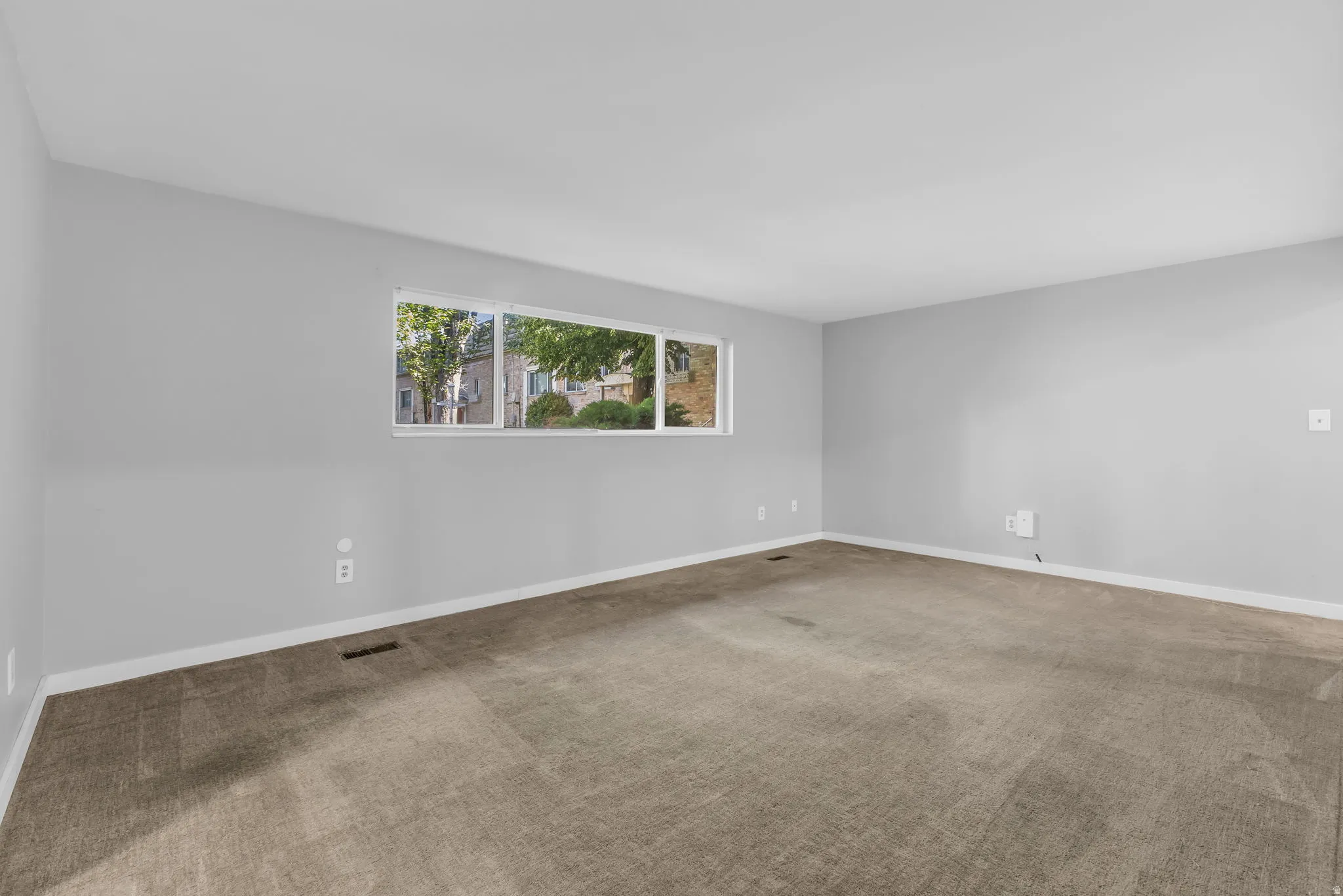 Spacious interior room featuring light gray wall paint, white trim, and neutral-toned carpeting