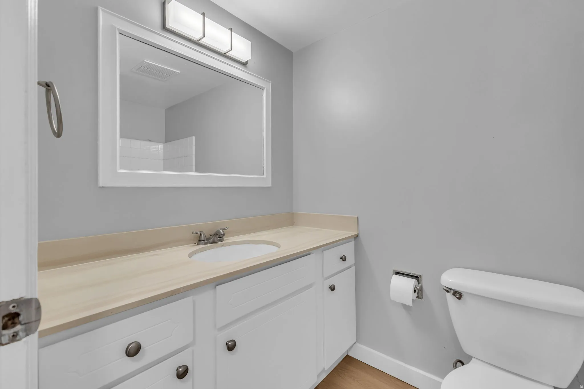 Bathroom featuring a single vanity with a light-colored countertop, white cabinetry with dark hardware, a framed mirror, and a wall-mounted light fixture
