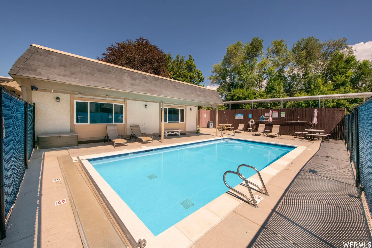 Outdoor swimming pool with concrete surround, perimeter fencing, and an adjacent building featuring a covered patio area