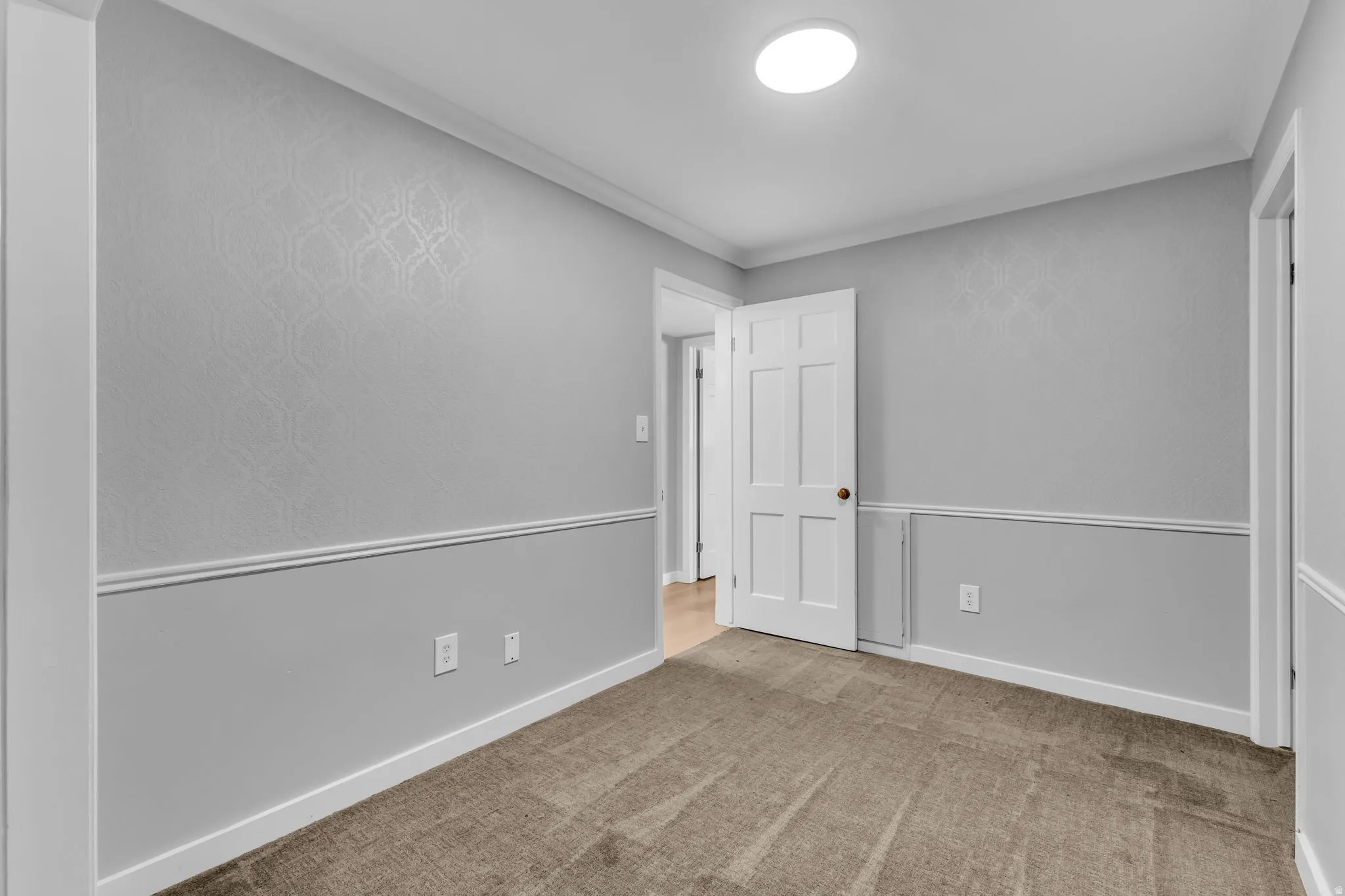 Neutral tone room featuring wall paneling, patterned wallpaper, a white paneled door, and overhead flush mount lighting