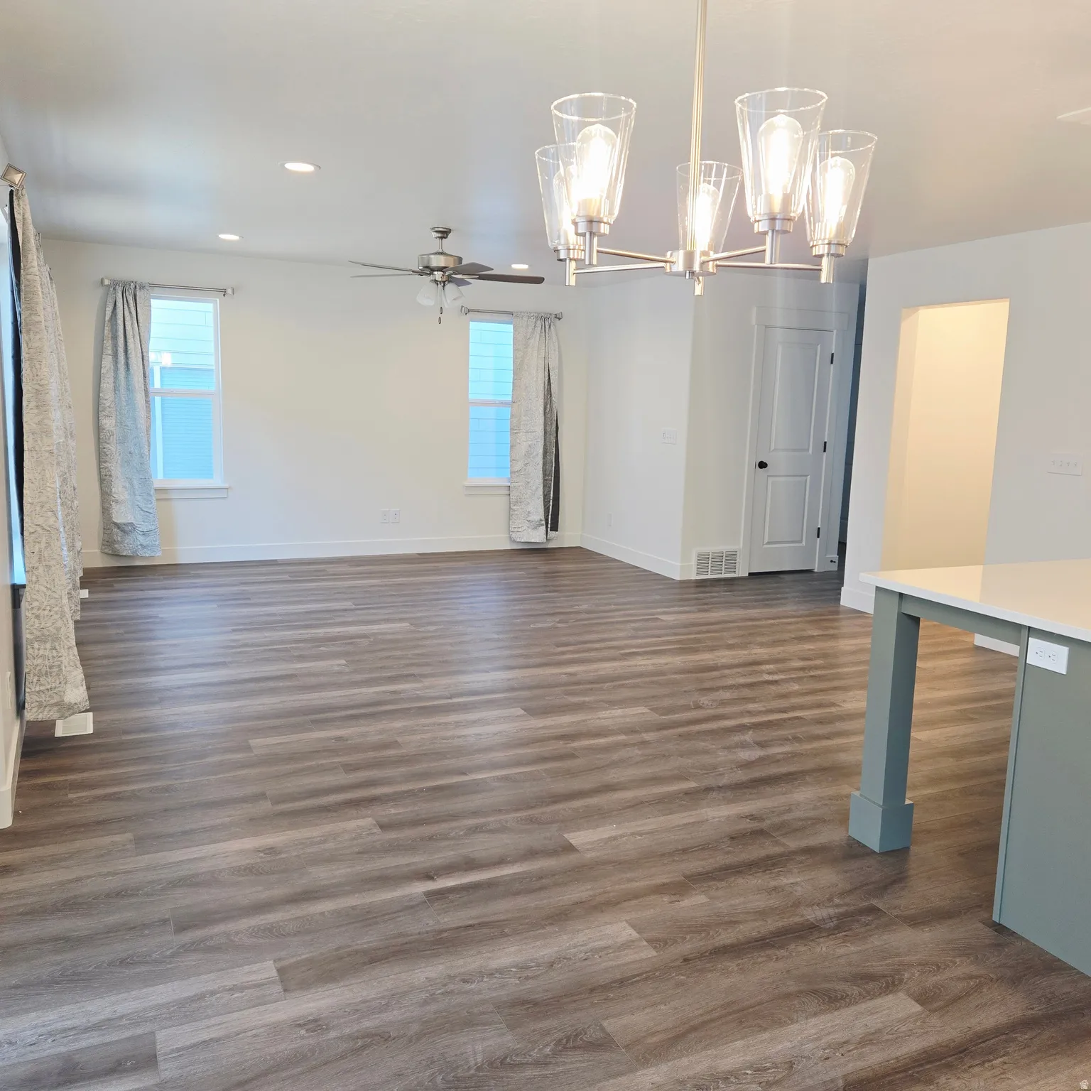 Spacious open-concept living area featuring wood-finish flooring, recessed lighting, and a contemporary chandelier