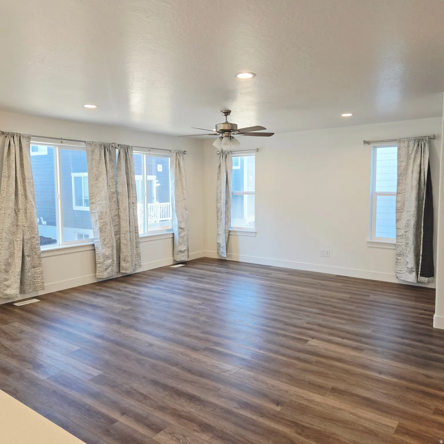 Spacious room featuring wood-finish flooring, white walls, multiple windows with white trim, recessed lighting, and a ceiling fan