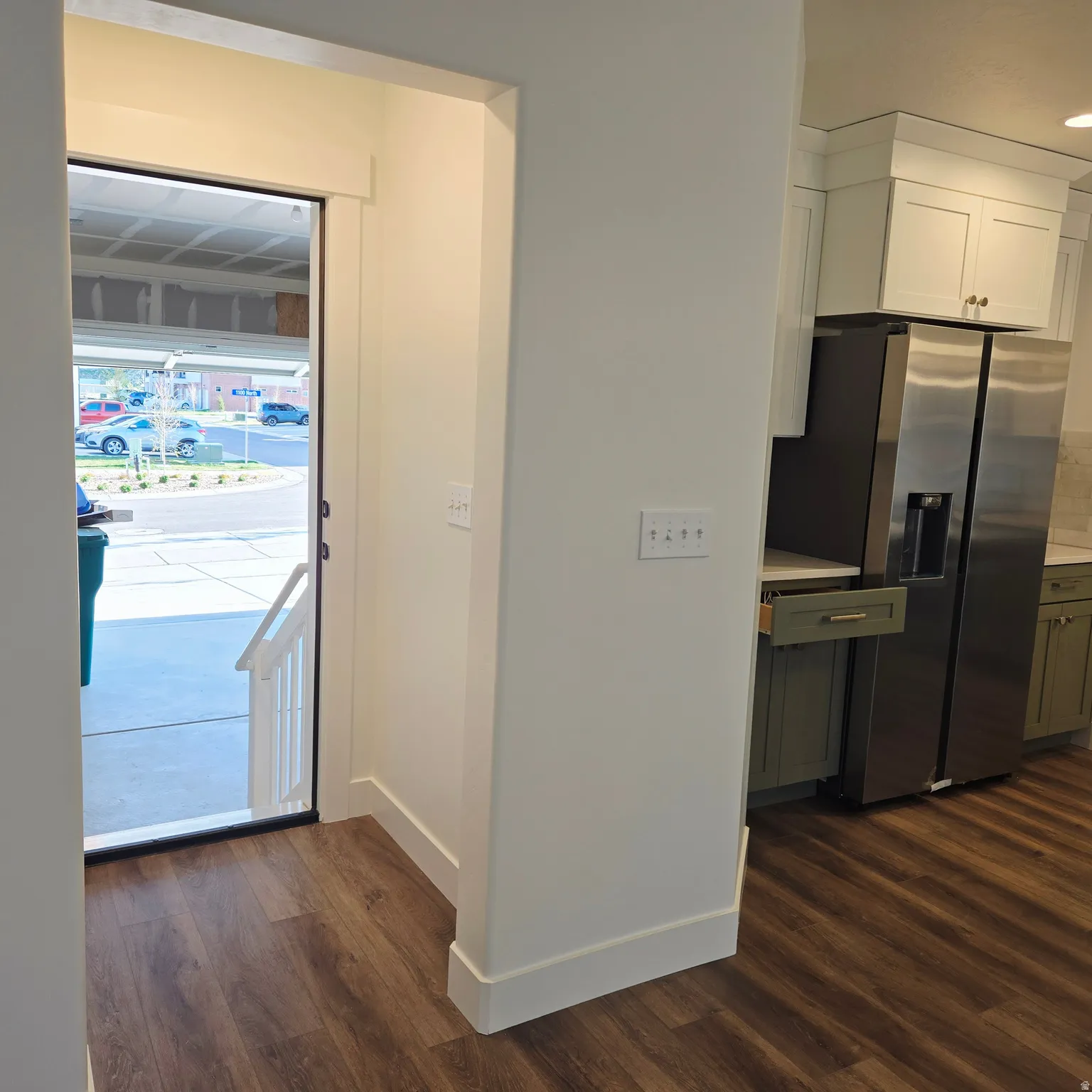 Wood-finish flooring throughout, bright white baseboards, and a modern kitchen featuring white upper cabinetry, sage lower cabinetry, and a stainless steel refrigerator