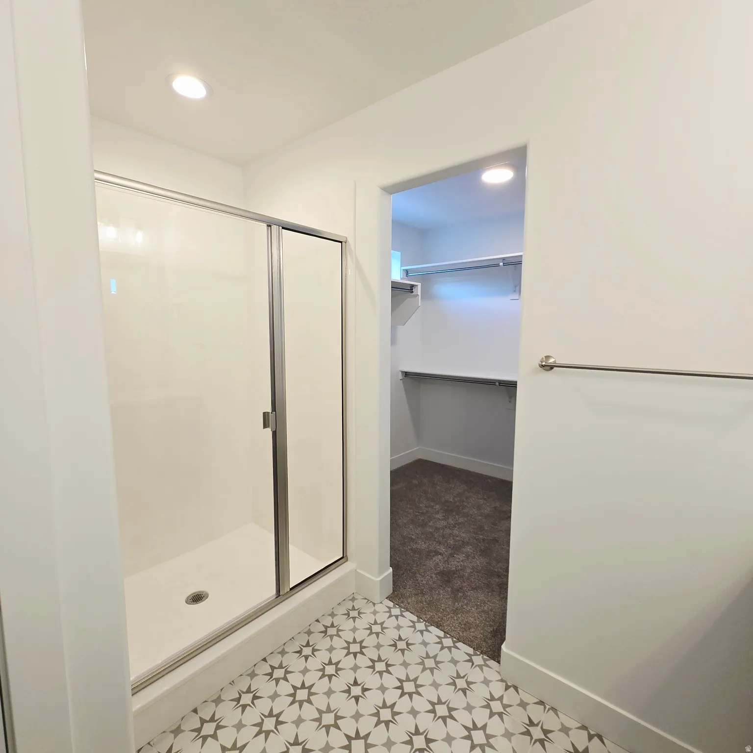 Walk-in shower with sliding glass door, patterned floor tiles, recessed lighting, and a closet entry with built-in shelving and carpet flooring