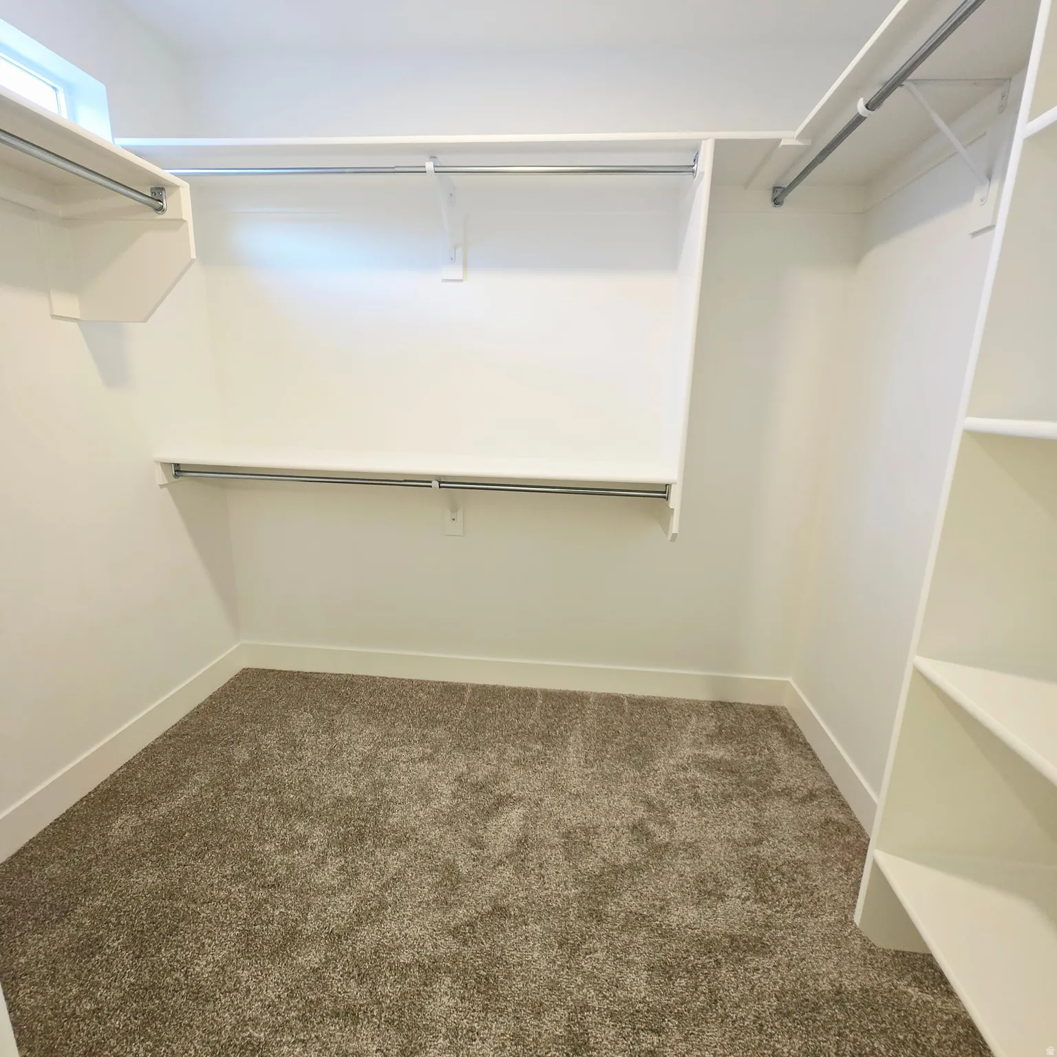 Custom closet system with multiple shelving tiers, hanging rods, built-in vertical storage, window providing natural light, and plush carpeting