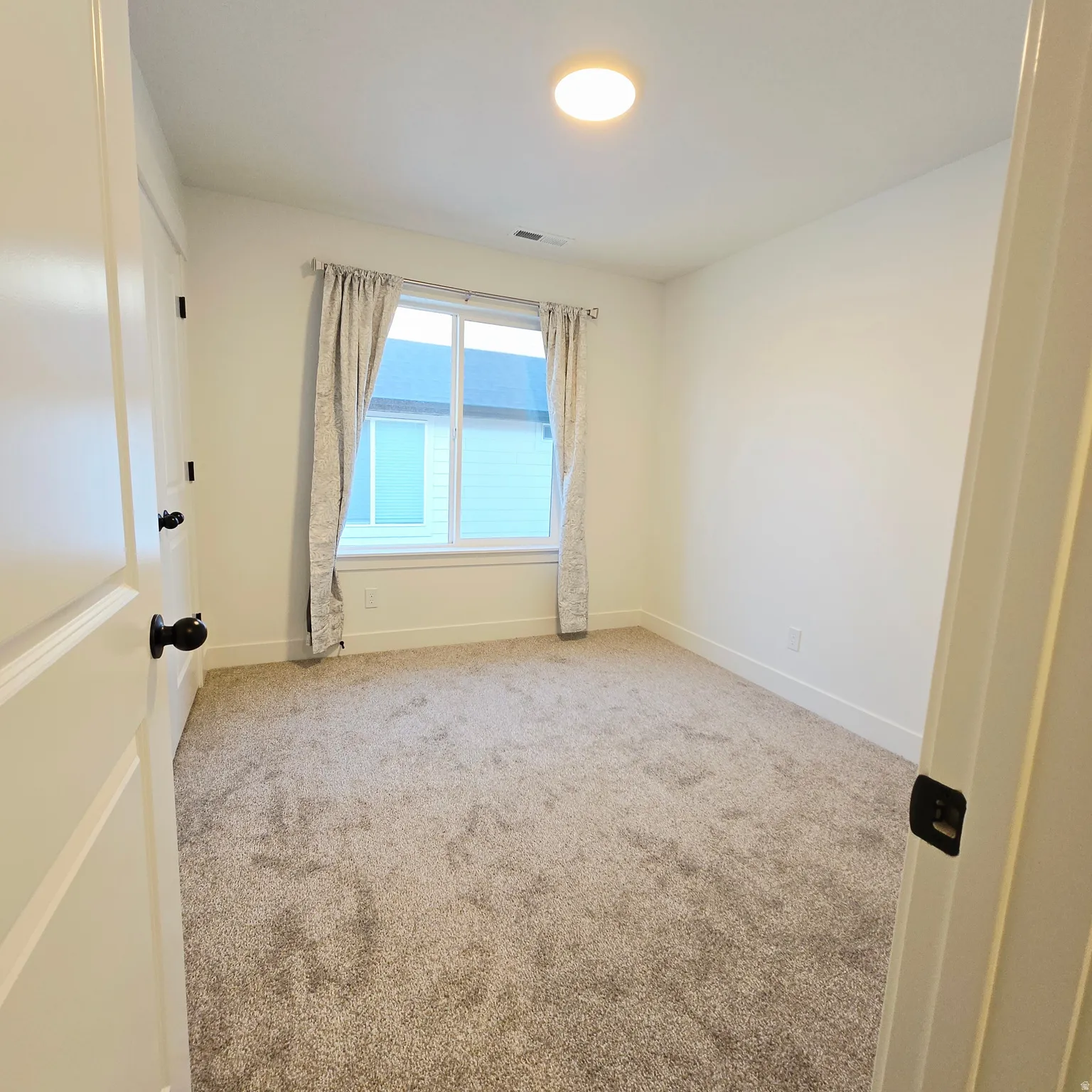 Carpeted room featuring a white window frame, contemporary flush-mount ceiling light, white baseboards, and white walls