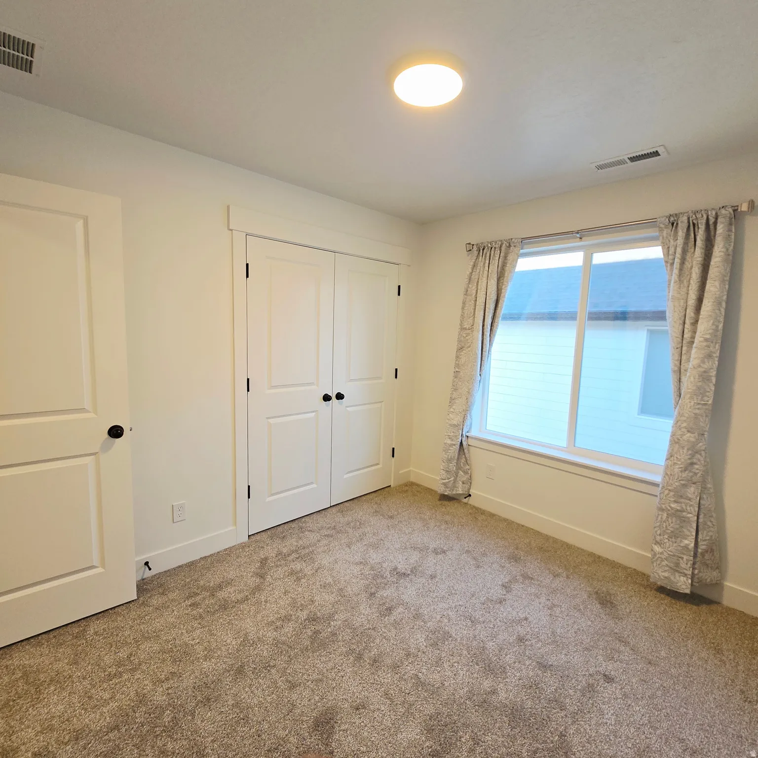 Carpeted room featuring a large window, double-door closet, and overhead lighting