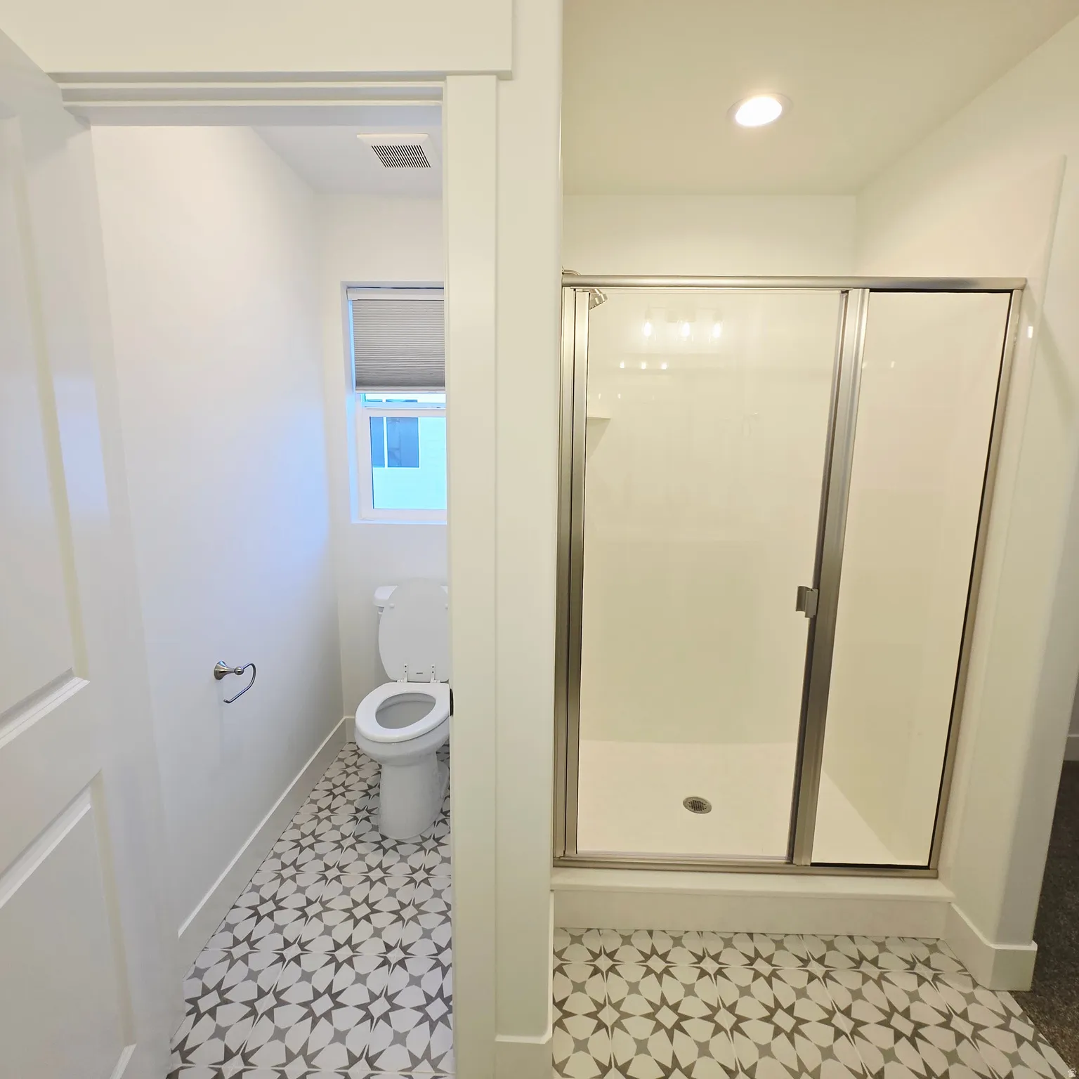 Bathroom featuring a glass-enclosed shower with a white surround, a toilet, and patterned floor tiles