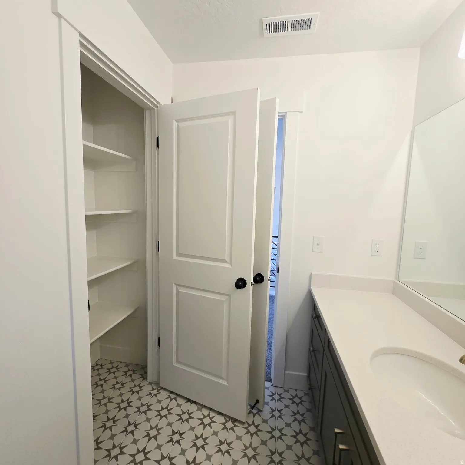 Bathroom featuring a patterned tile floor, built-in shelving, dark gray vanity with a single basin, and a light-toned countertop