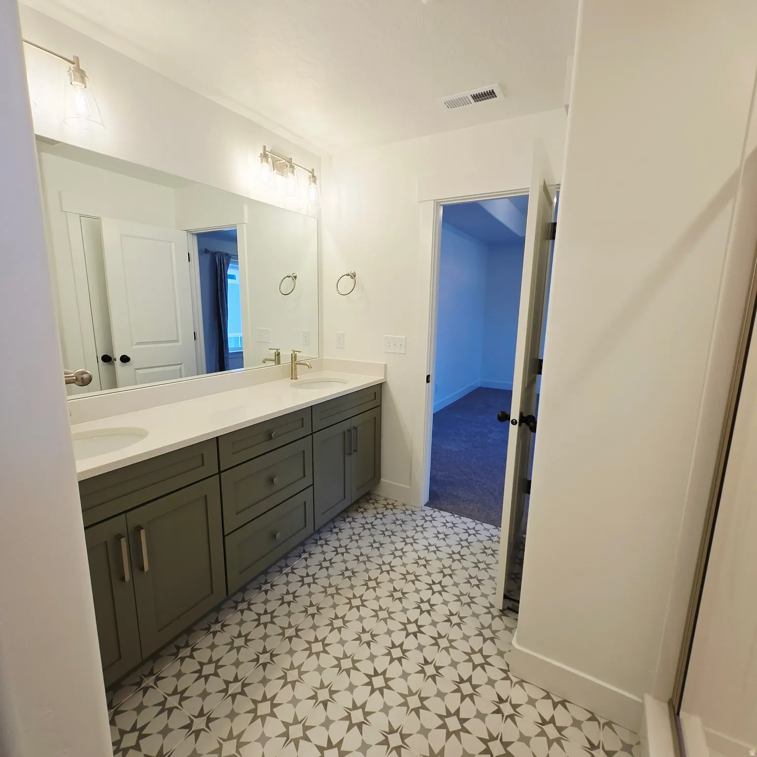 Bathroom featuring a dual vanity with a light countertop, gray cabinetry, patterned floor tiles, and contemporary wall-mounted light fixtures