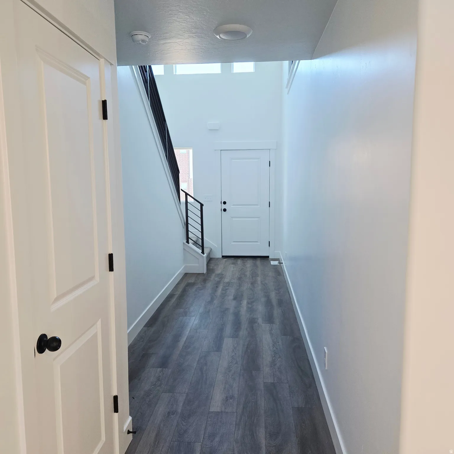 Entryway featuring wood-finish flooring, white paneled doors, a modern black metal staircase railing, and recessed lighting