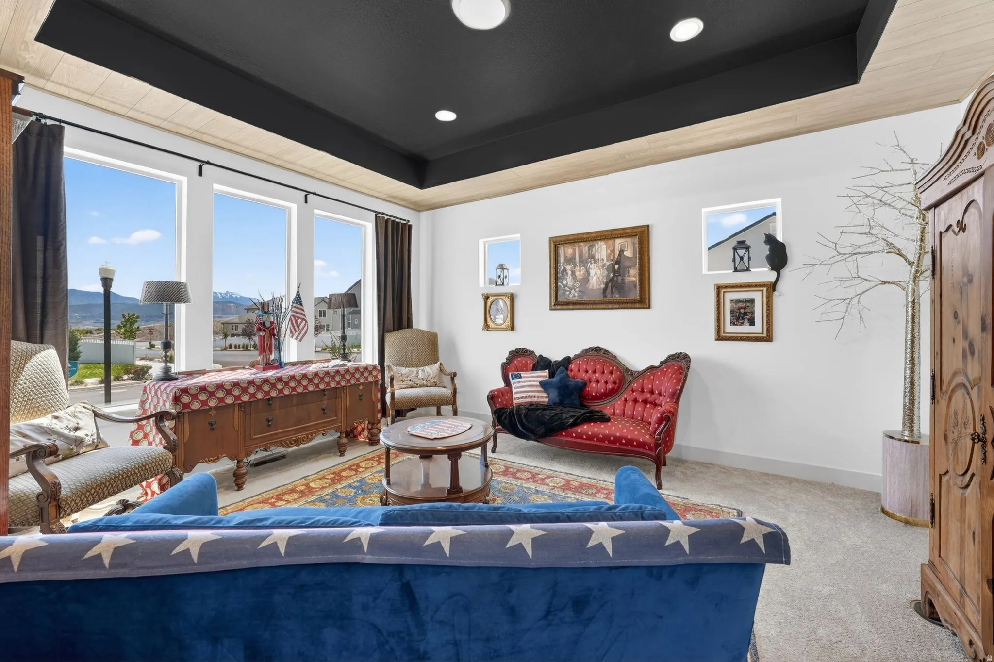 Spacious living area featuring large picture windows, a tray ceiling with recessed lighting, and light-toned carpeting