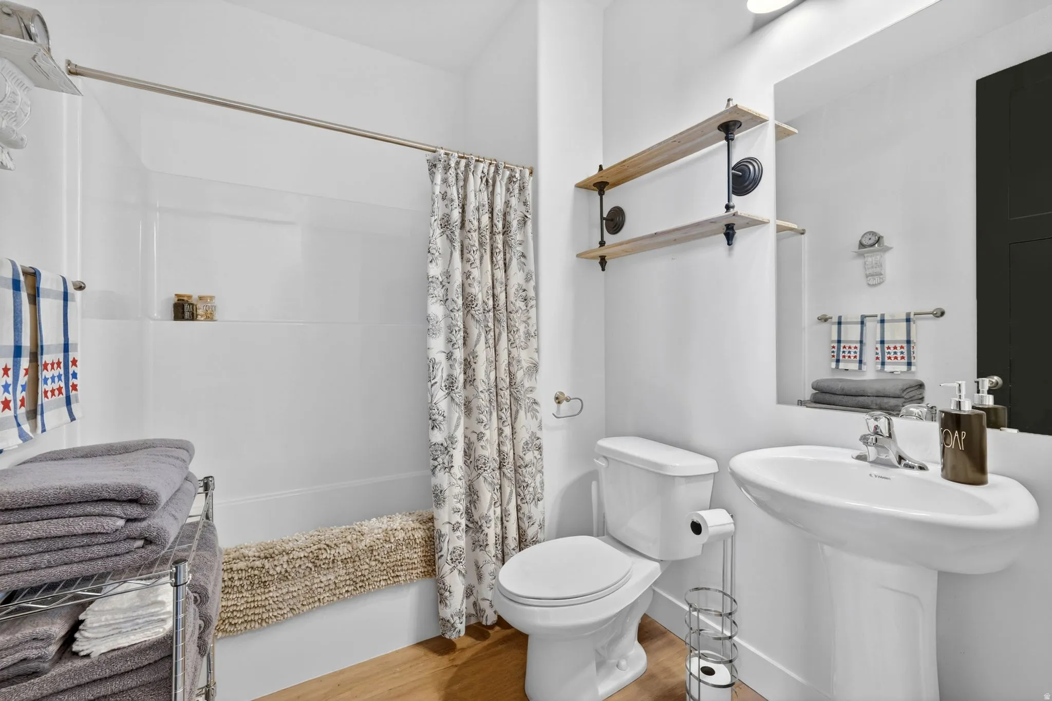 Bathroom featuring a white pedestal sink with a chrome faucet, a white toilet, and wood-finish flooring
