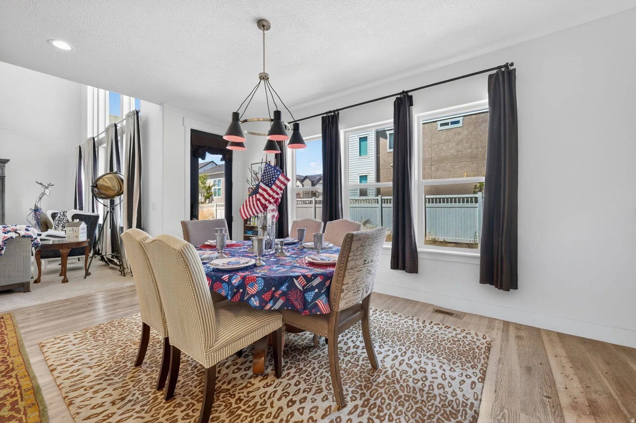 Dining area featuring wood-finish flooring, a modern chandelier with black and red accents, and multiple windows with dark drapery