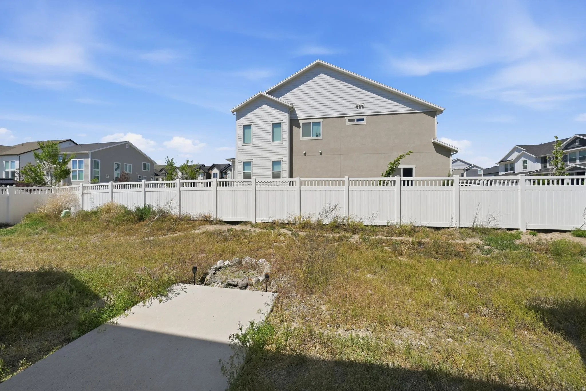 Spacious yard area with a partial concrete pad and a white privacy fence