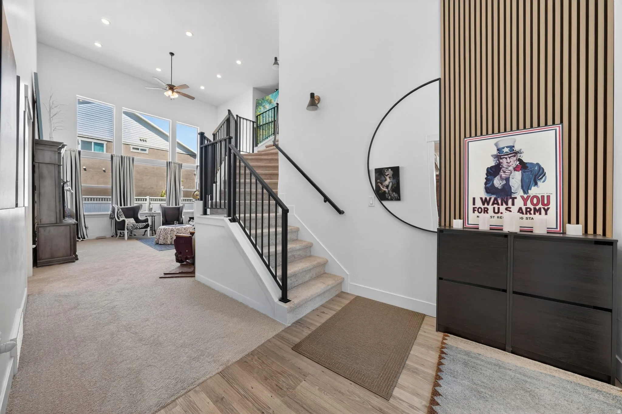 Entryway featuring wood-finish flooring transitioning to carpet, a staircase with black metal railings, and a vertical wood slat accent wall