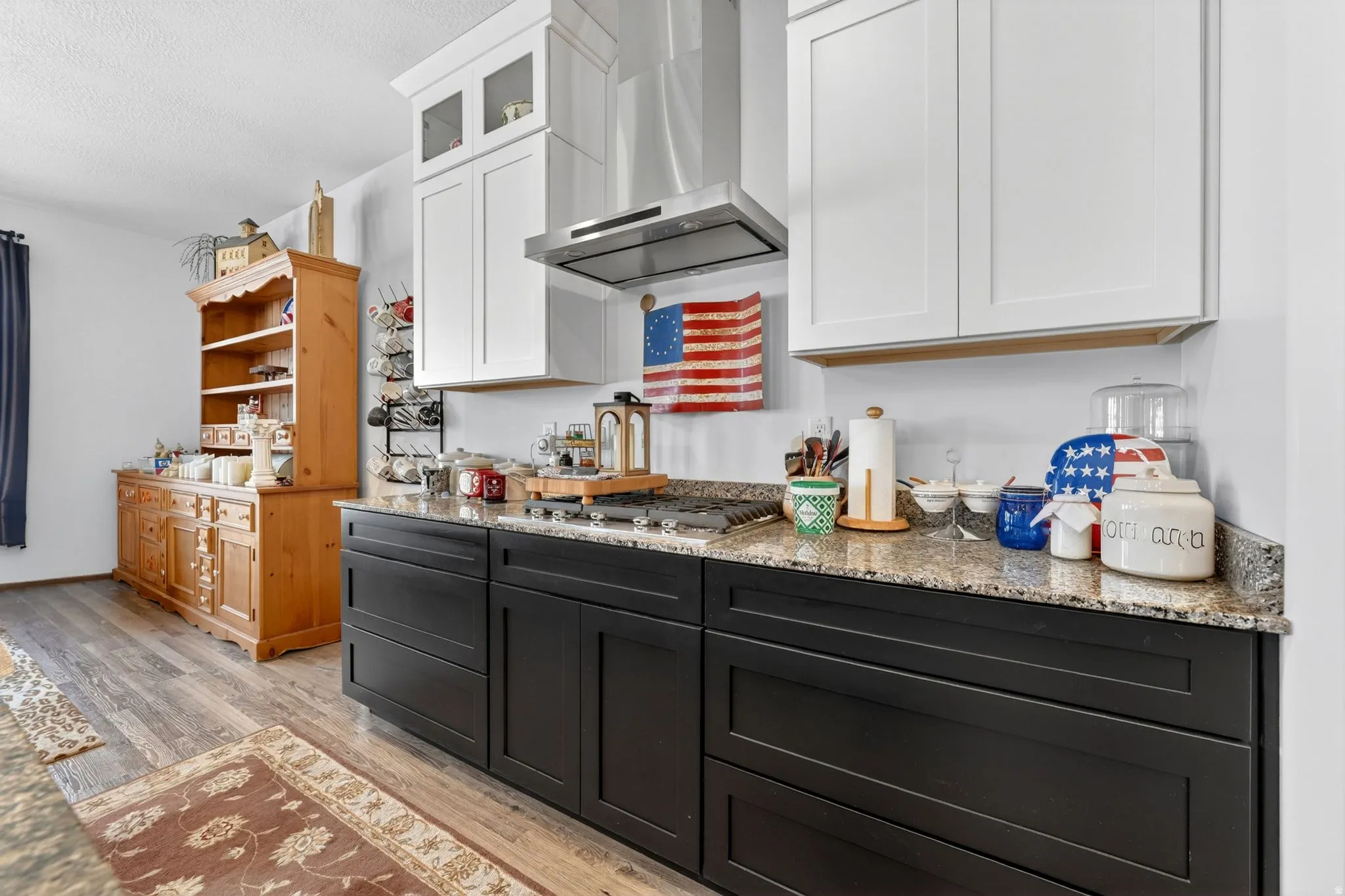 Kitchen with two-tone cabinetry featuring white upper cabinets and dark lower cabinets, granite countertops, and a stainless steel range hood
