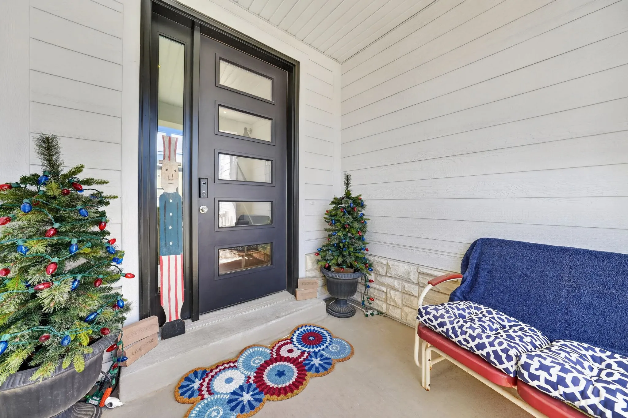 Modern front entry featuring a black multi-paneled door, sidelight, and light-colored horizontal siding