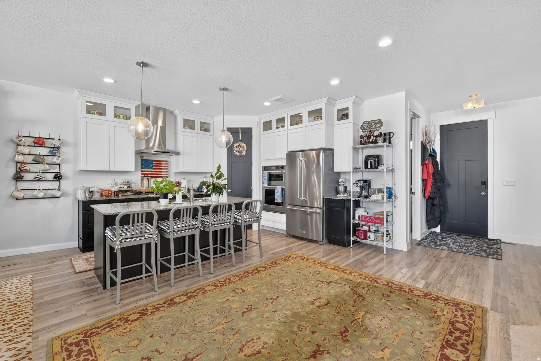 Spacious kitchen featuring a large island with seating, stainless steel appliances, white upper cabinetry with glass inserts, and wood-finish flooring