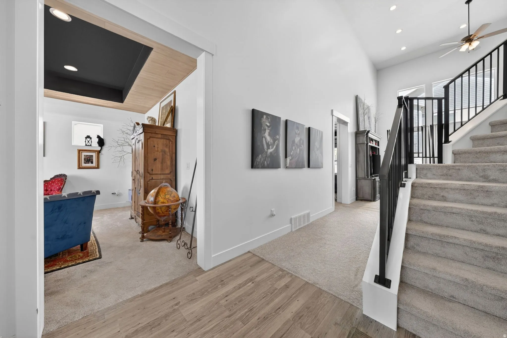 Main level hall featuring wood-finish flooring, a carpeted staircase with dark metal railings, and a recessed ceiling with wood paneling and black accent
