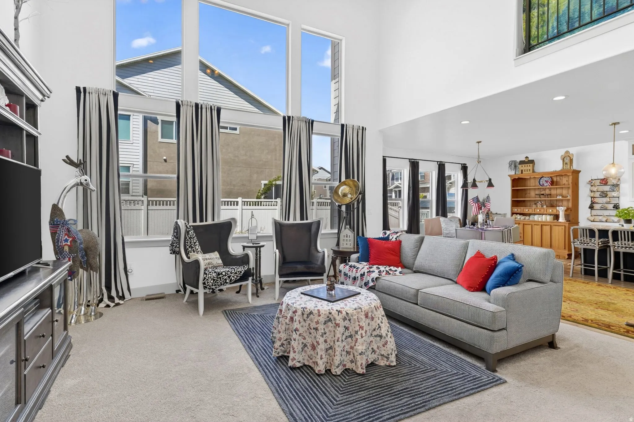 Living room featuring soaring ceilings, a wall of multi-pane windows, light-colored carpeting, a built-in entertainment center, and an open concept layout with an adjacent dining area