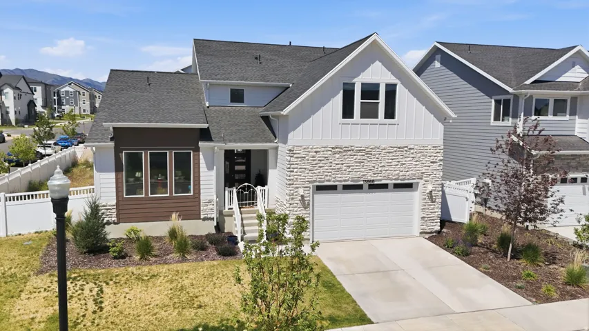 Modern farmhouse-style residence featuring a combination of white vertical siding, horizontal brown siding, and stone veneer accents