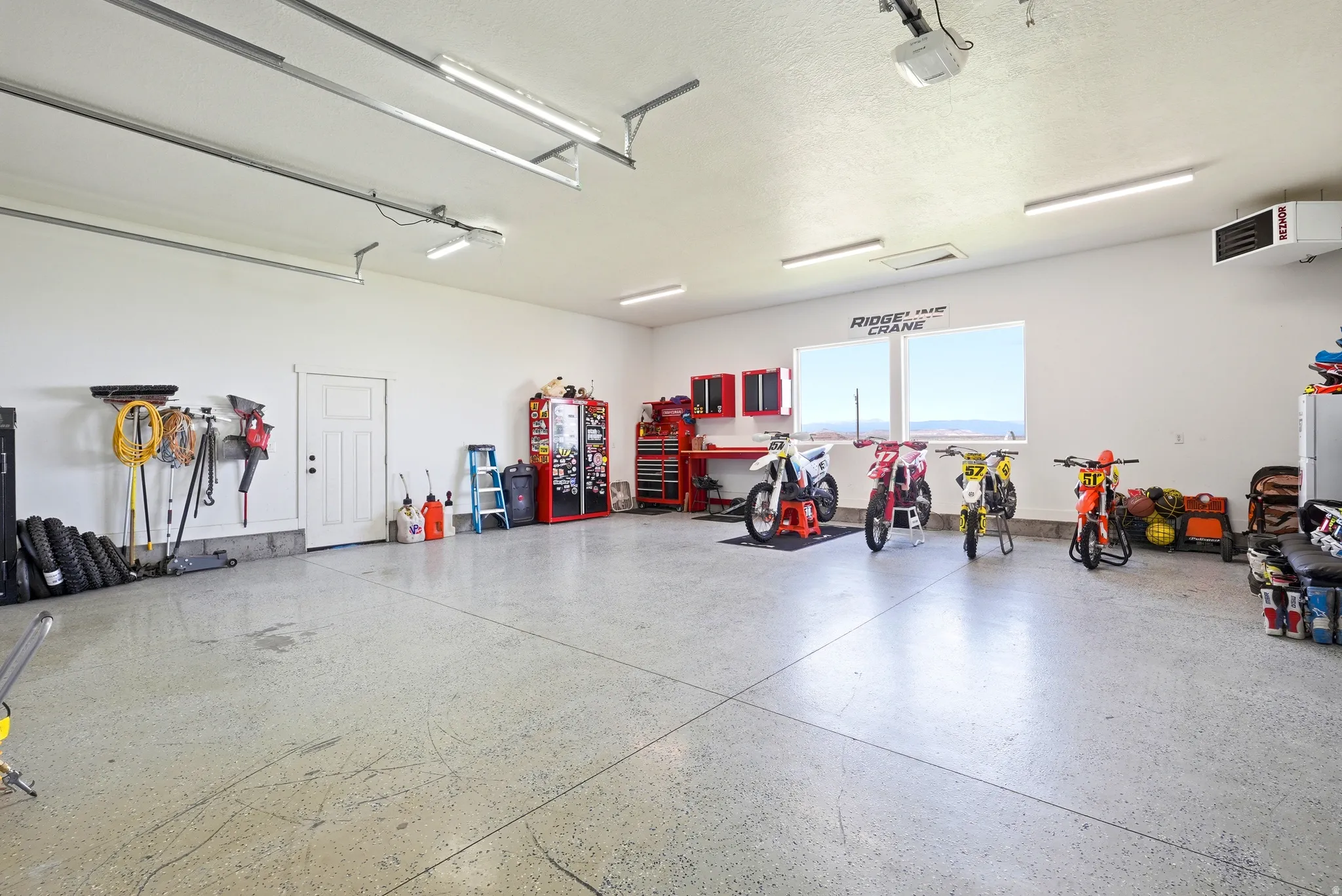 Spacious garage with light-colored concrete flooring, multiple fluorescent light fixtures, and a large window providing natural light