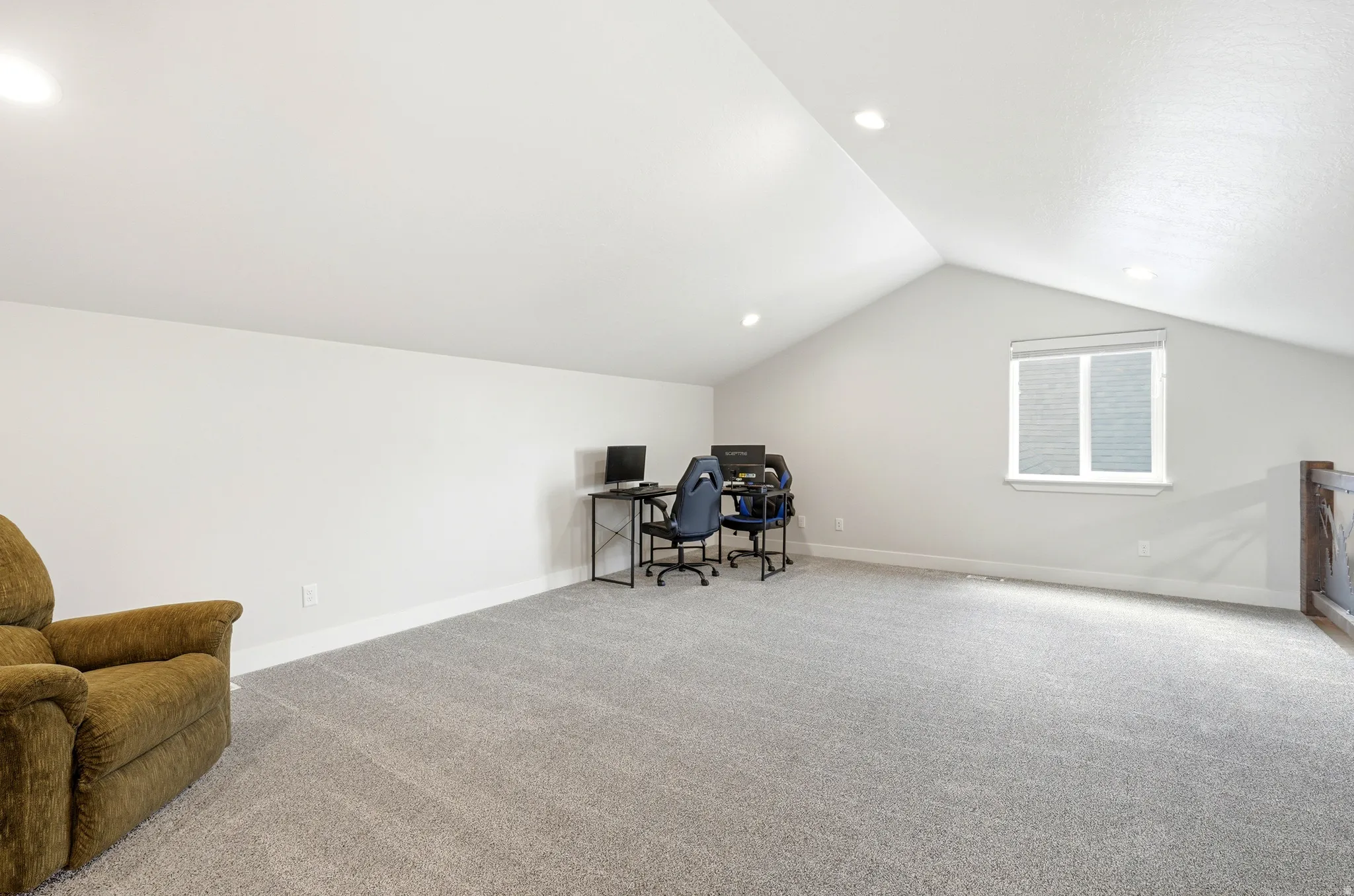 Spacious carpeted room featuring a vaulted ceiling with recessed lighting