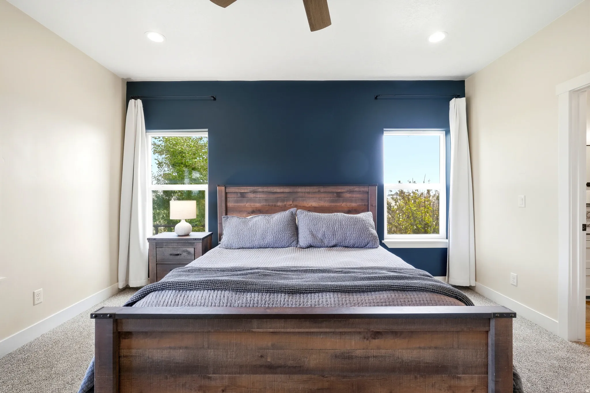 Bedroom with a striking dark accent wall, two large windows, recessed lighting, and a ceiling fan