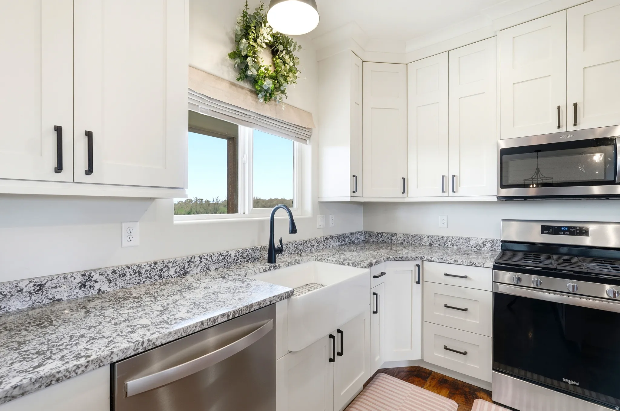 Kitchen featuring white shaker-style cabinetry with black hardware, light-toned stone countertops, and a white farmhouse sink