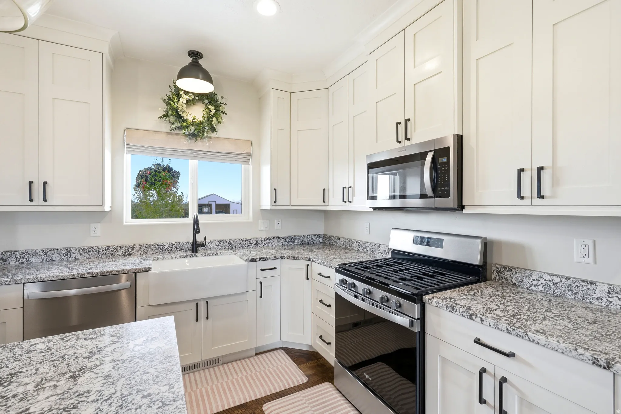 Modern kitchen featuring white shaker-style cabinetry with matte black hardware, speckled granite countertops, stainless steel appliances, and a farmhouse-style sink with a matte black faucet