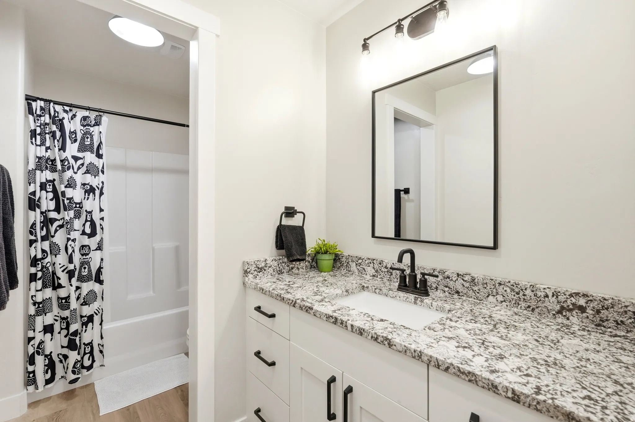 Full bathroom featuring a white vanity with a speckled countertop, integrated sink, and matte black faucet