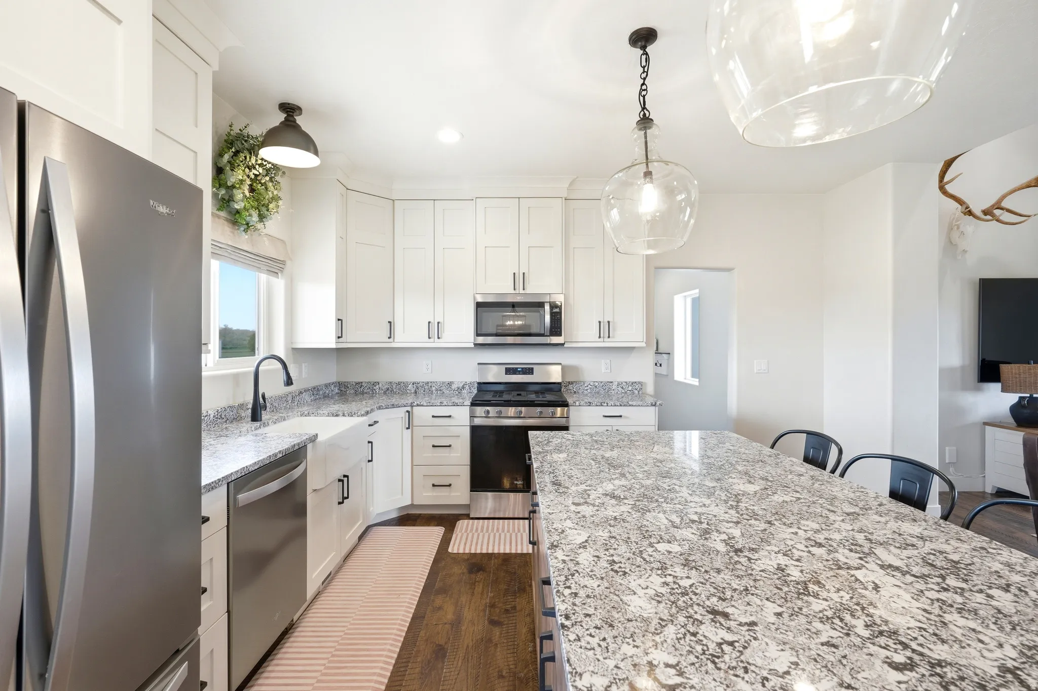 Kitchen featuring a large island with granite-style countertop, white cabinetry with dark hardware, stainless steel appliances, and wood-finish flooring