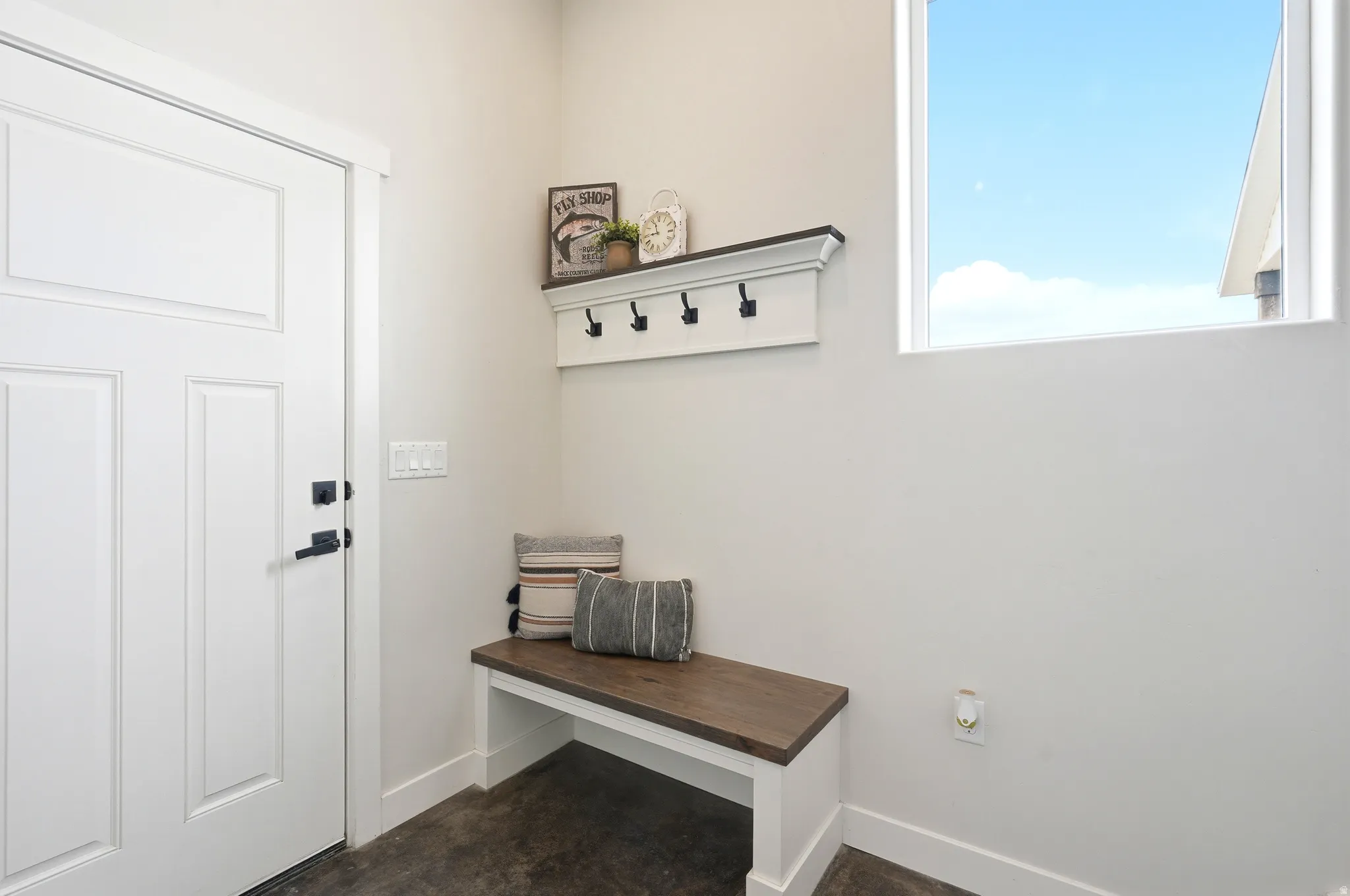 Entryway featuring a white paneled door with matte black hardware, built-in mudroom bench with wood-finish top, white wall-mounted shelf with black hooks, and a rectangular window