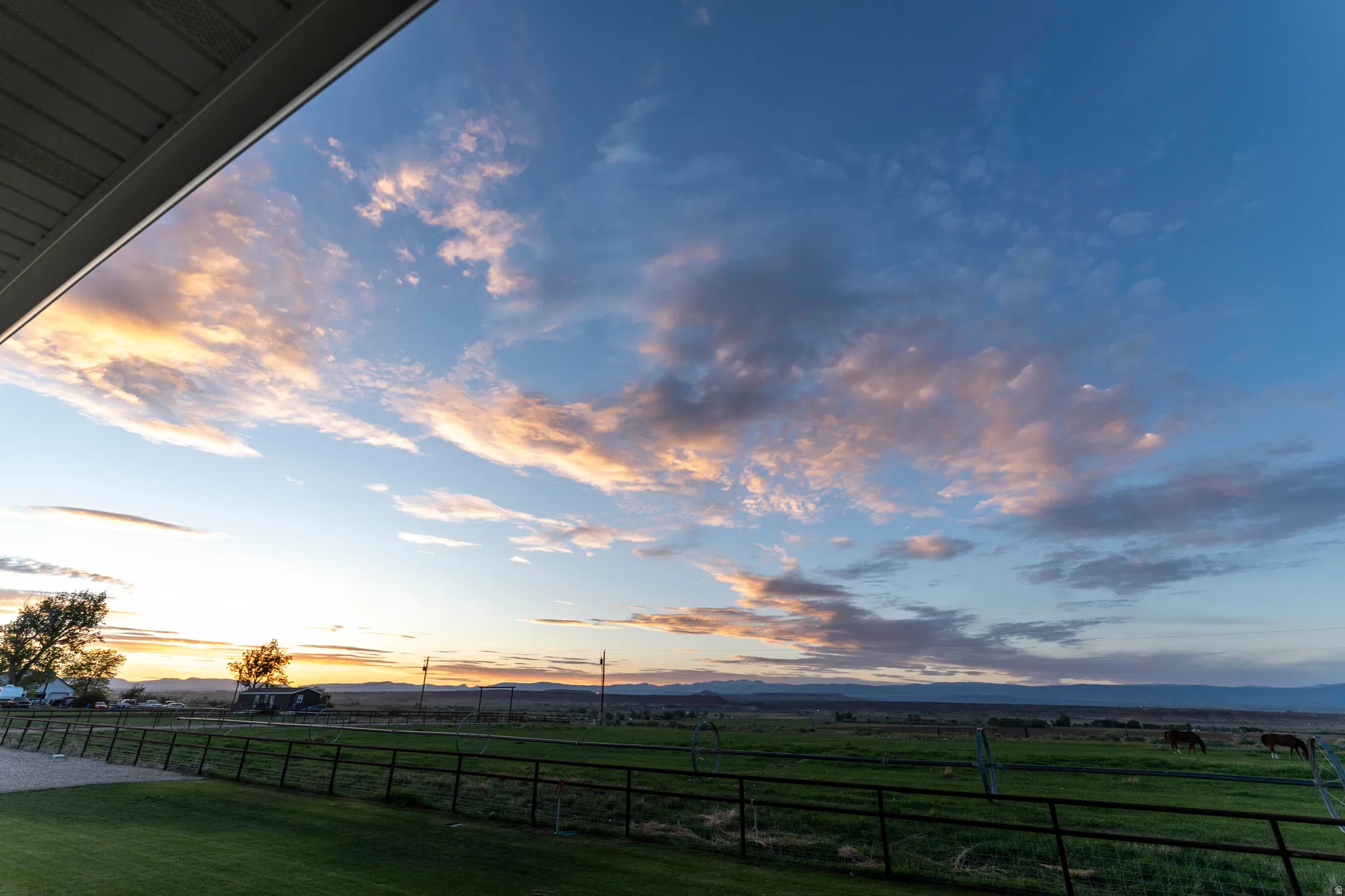 Expansive outdoor space featuring a manicured lawn, perimeter fencing, and distant mountain ranges