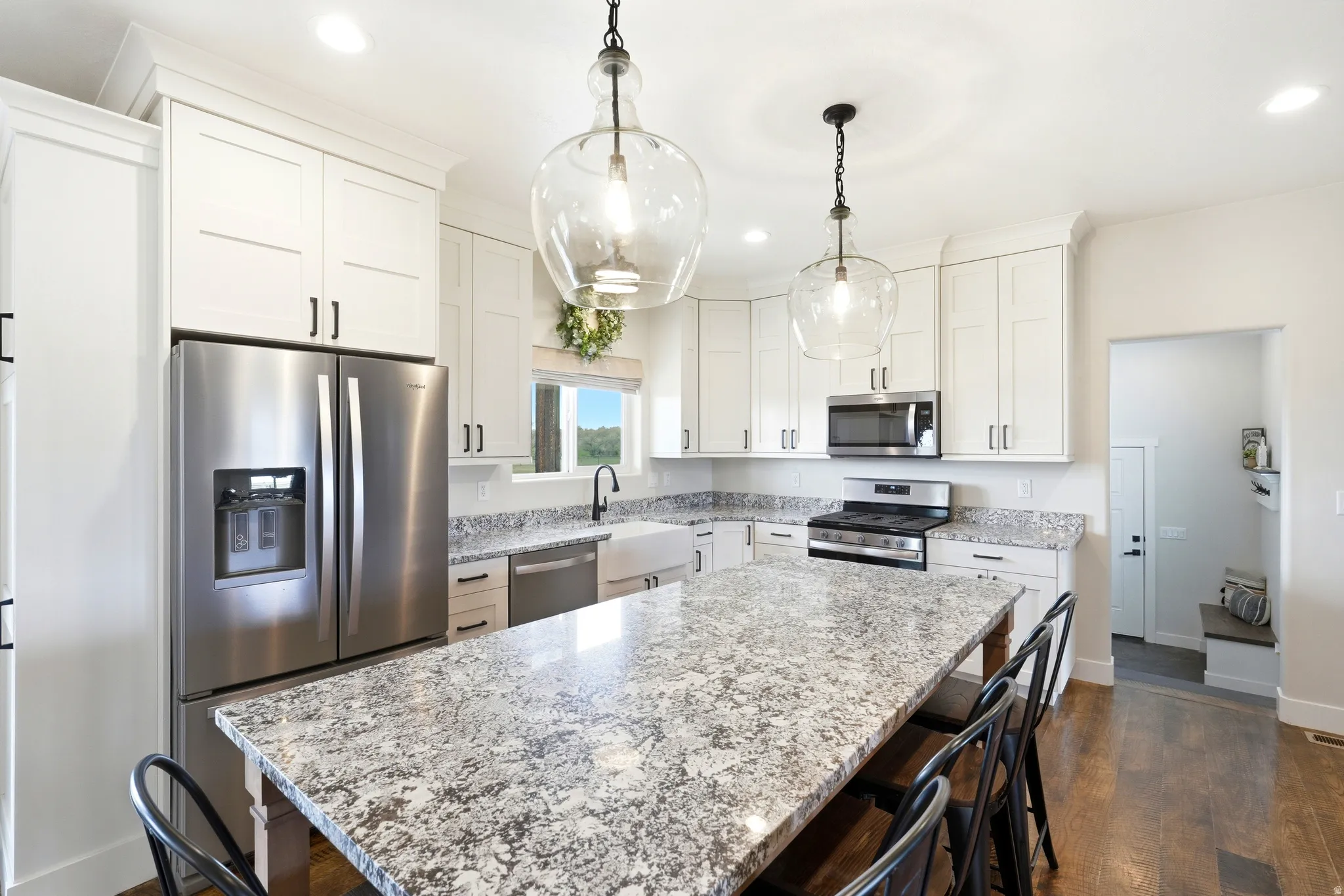 Kitchen featuring a large central island with seating, white shaker-style cabinetry, stainless steel appliances, and pendant lighting