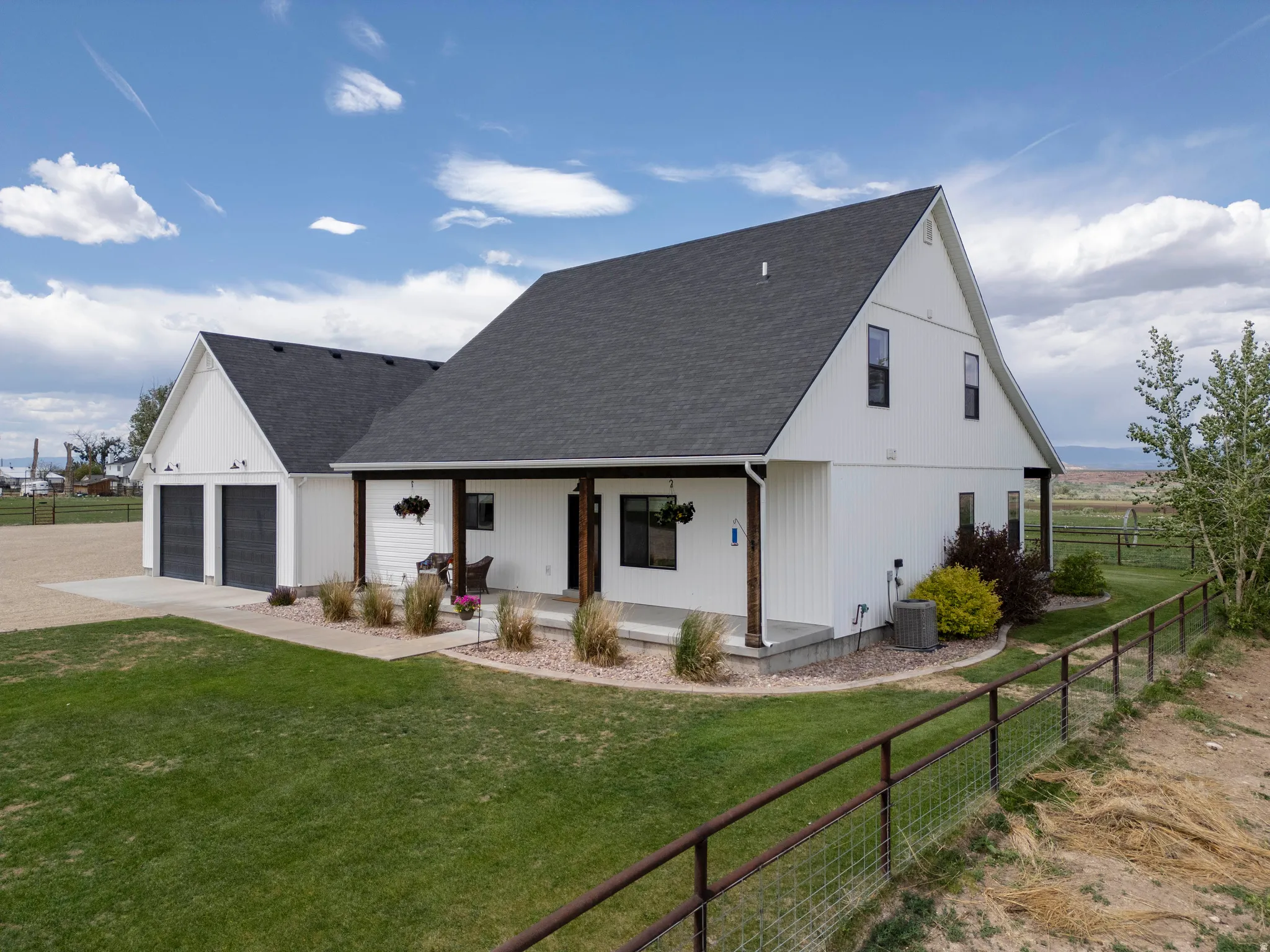 Modern farmhouse architecture featuring white vertical siding, a dark pitched roof, and a covered porch with dark wood columns