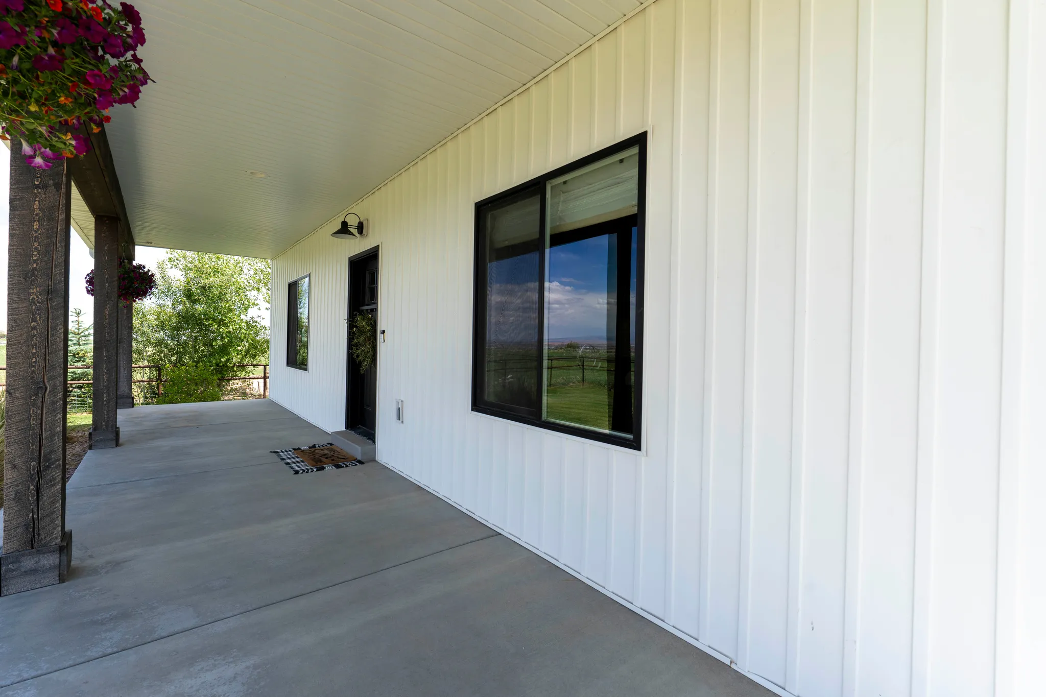 Covered concrete porch featuring rustic wood columns and a white vertical panel exterior