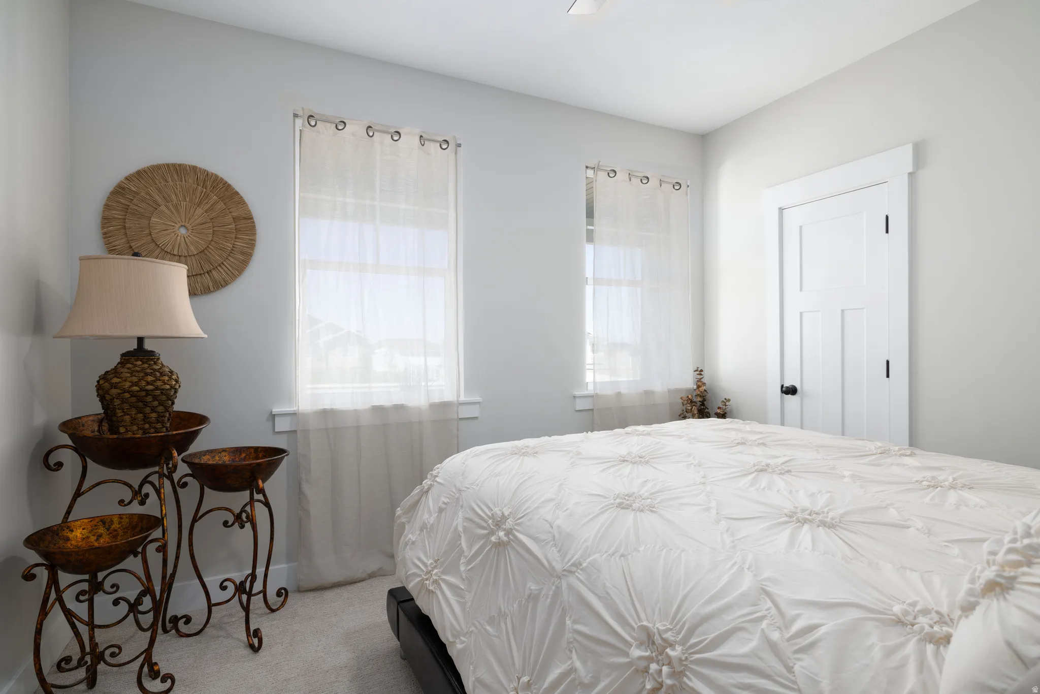 Light-filled room featuring two windows with white trim, a three-panel door with black hardware, and neutral-toned wall-to-wall carpeting
