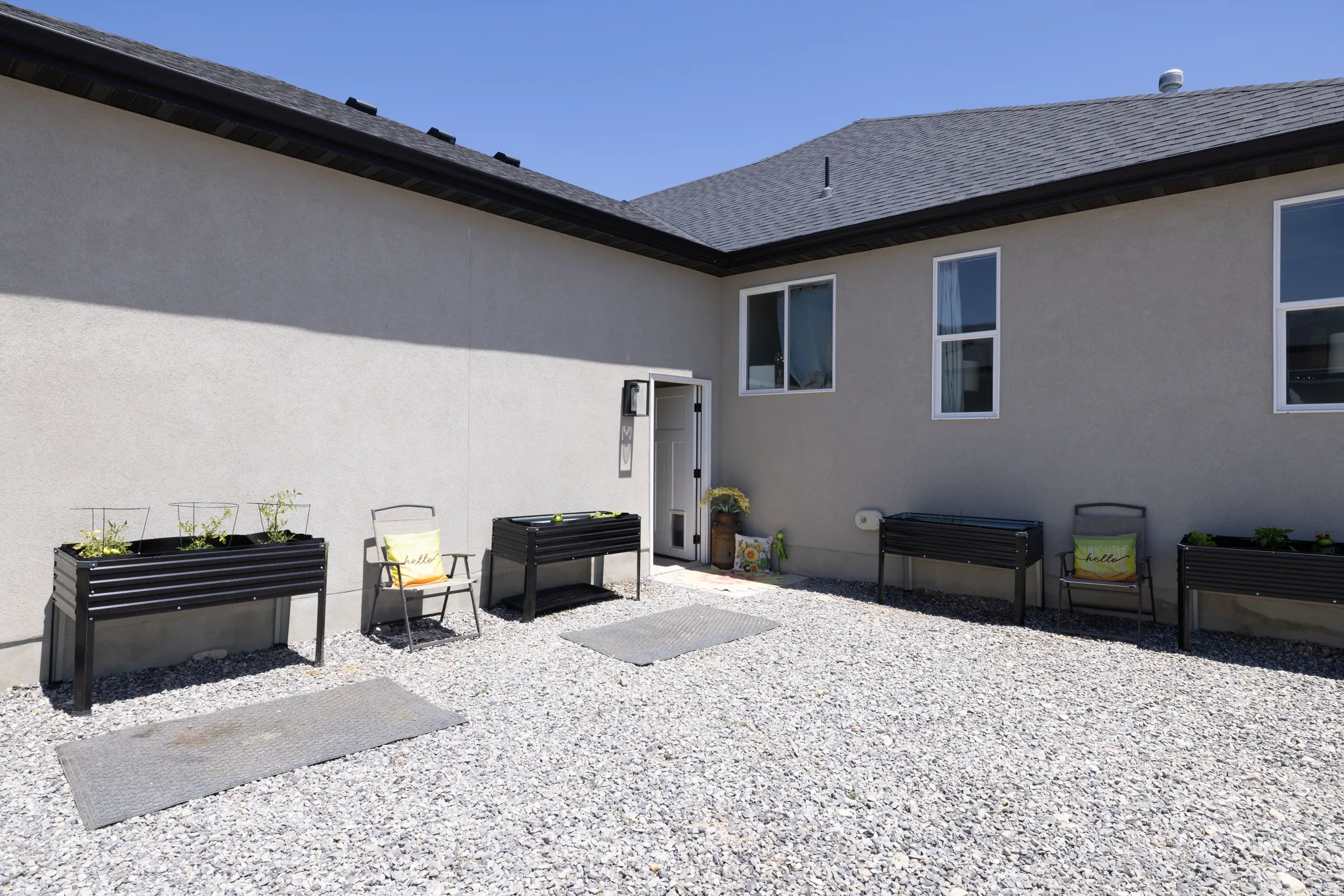 Low-maintenance exterior featuring a gravel patio, stucco siding, and a dark shingle roof