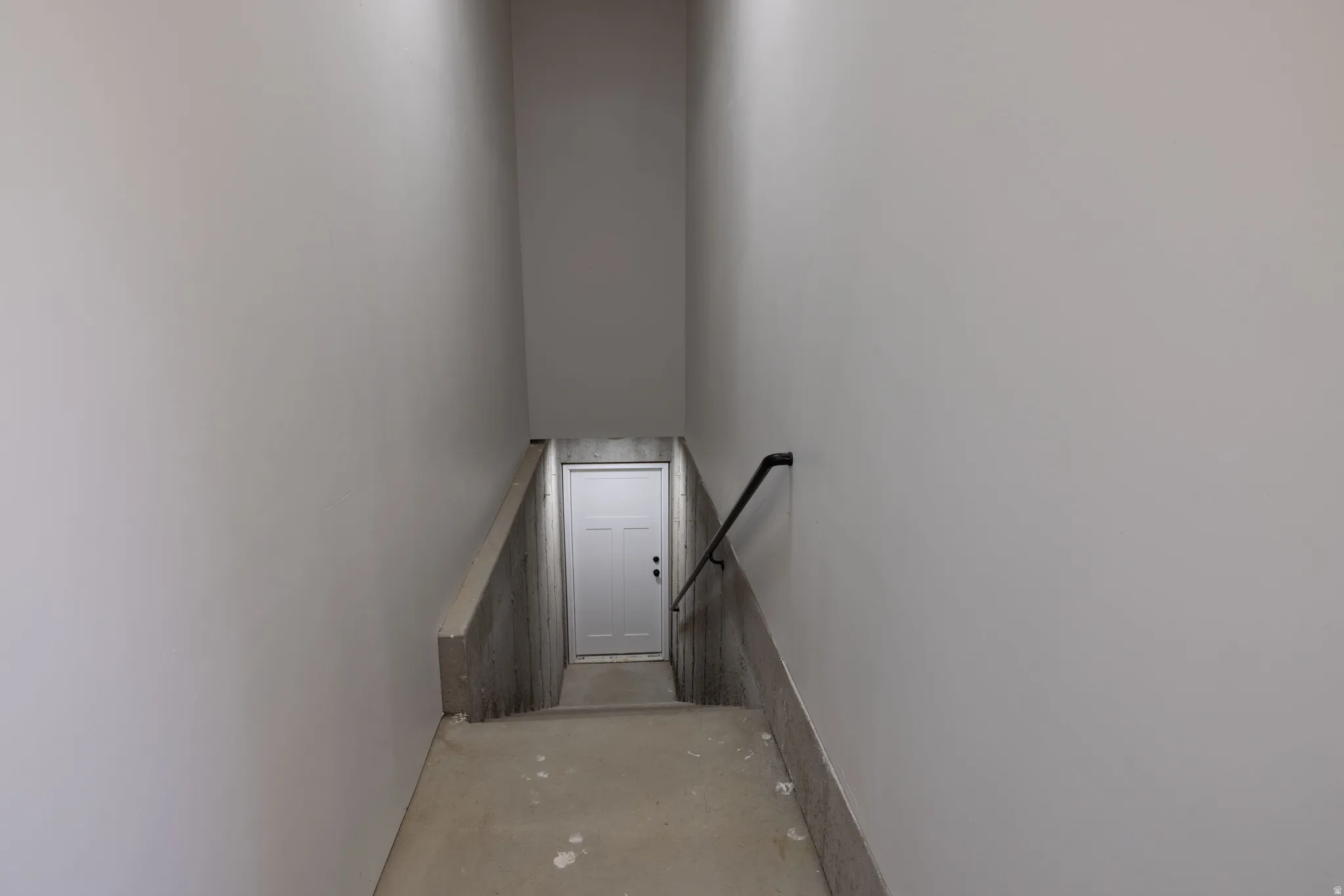 ADU/Basement entrance from Garage.  Stairwell with unfinished concrete steps, a white paneled door, and a black handrail