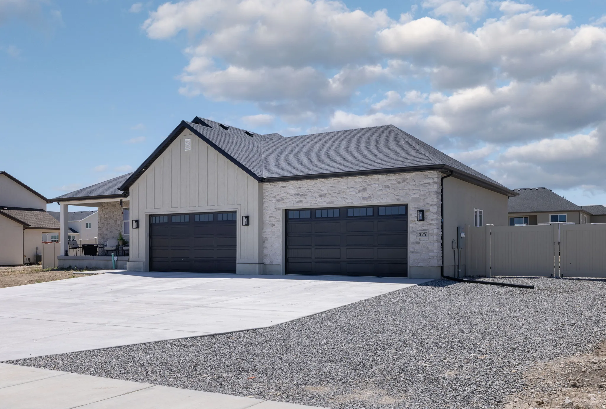 Contemporary exterior featuring a board and batten gable, light-toned stone veneer, and a dark asphalt shingle roof